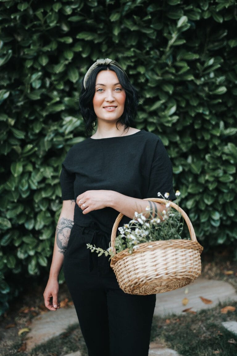 Cassidy Moss holding a basket of fresh herbs in front of a green hedge