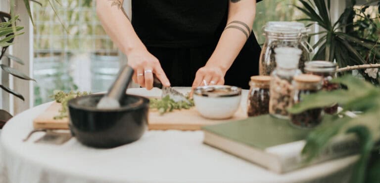Hands grinding herbs in a mortar at the worktable