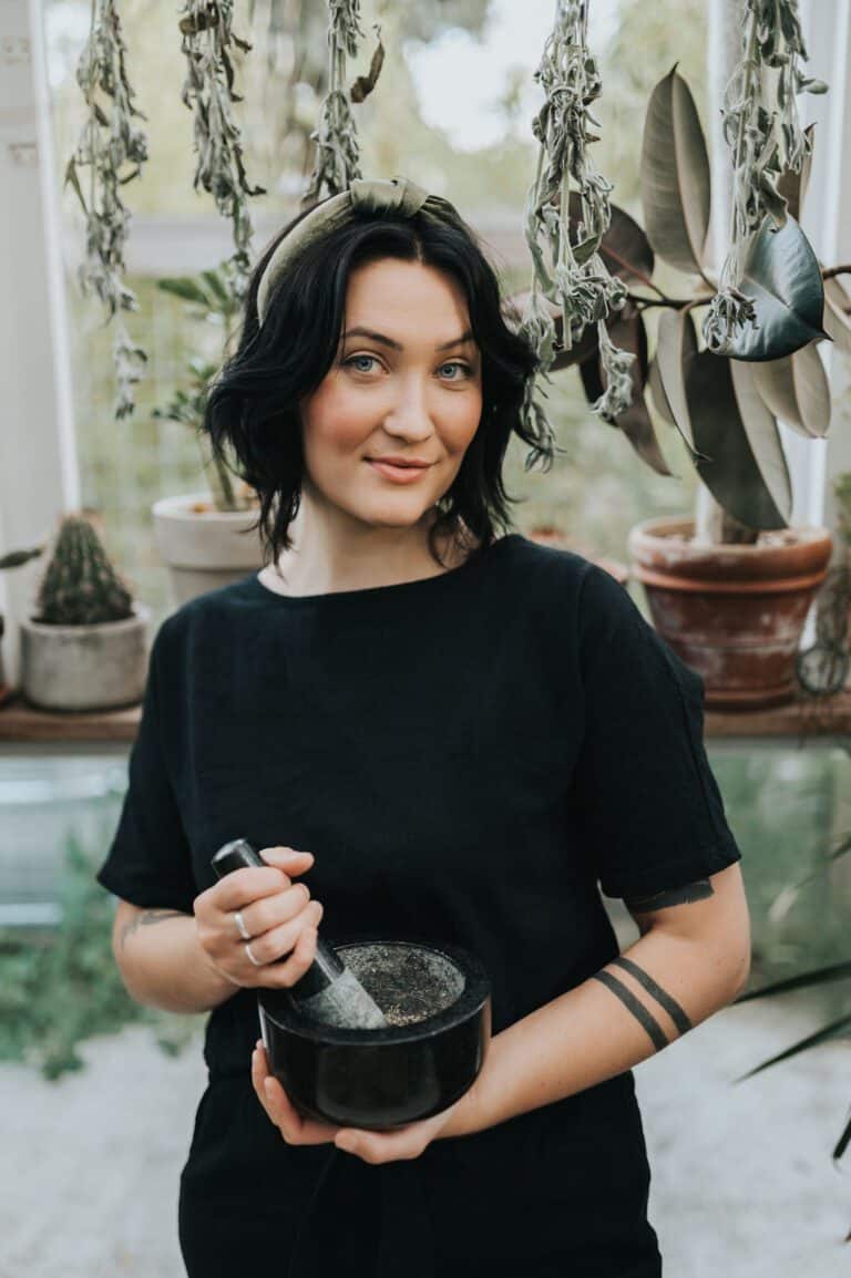 Cassidy Moss smiling in the greenhouse, holding a mortar and pestle