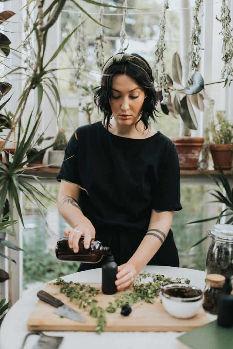Cassidy pouring a tincture at a table of fresh herbs in the greenhouse