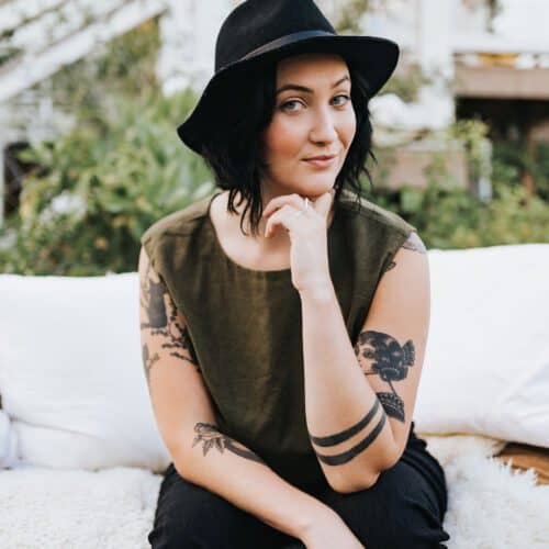 Cassidy Moss, clinical herbalist, seated outdoors in a black hat