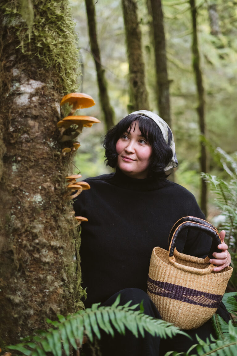 Cassidy Moss in the forest with a woven basket, beside a mossy tree with mushrooms