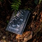 The Herbarium Vol. 2 resting on the forest floor beneath a fern
